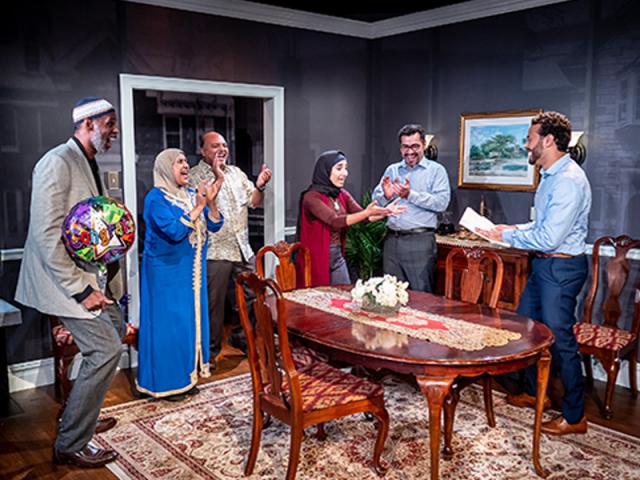 A Muslim family gathered around a table are excited. A man hands a paper to a woman