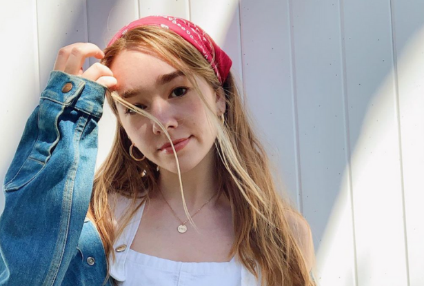 Holly Taylor in a red bandana, white shirt and jeans jacket, in front of a white wood frame wall.