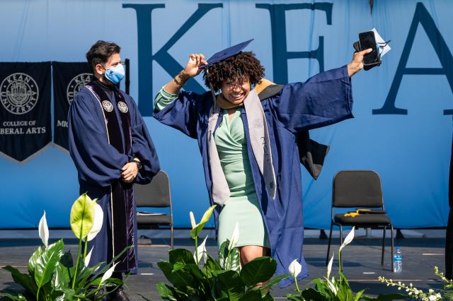 A woman in cap and gown celebrates as she walks across stage at one of Kean University's commencement ceremonies.
