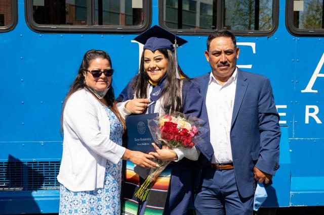 Kean grad with their family, holding flowers, in front of the Kean trolley