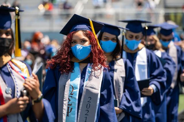 Image of students lined up to graduate from Kean, starting with a student with long curly red hair and blue mask.