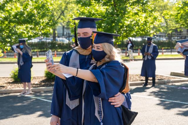 A sideview of two Kean graduates in their regalia taking a selfie