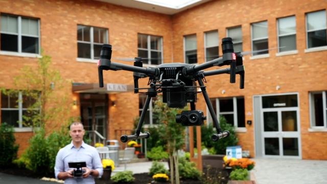 A man operates a drone outside a brick building on the Kean Skylands campus.