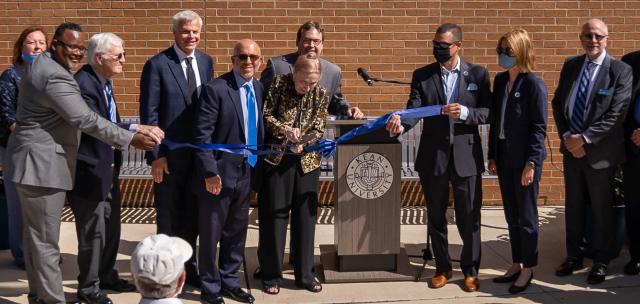 Distinguished Professor Emerita Dorothy Hennings cuts a blue ribbon while Kean University President Lamont Repollet and others look on.