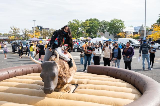 A student riding a mechanical bull and a crowd of students watching at Homecoming 2021.