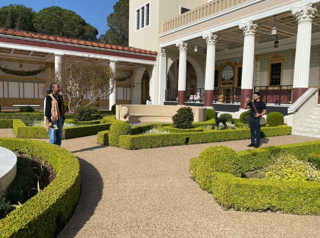 Nazira Goldware and Brandon Bravo taking photos of a garden for their internship. The garden is carefully structured and symmetrically shaped greenery that has a walkway made of pebbles.