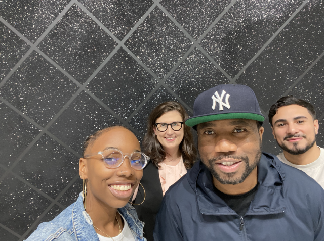 Nazira Goldware, Brandon Bravo, Knowledge Bennett, and Lynette Zimmerman smiling for a photo in front of Bennett's artwork, PIECES OF MAN.