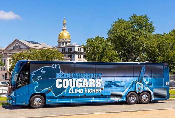 A Kean bus with the words, "Kean Cougars Climb Higher," with the N.J. State Capitol dome in the background.