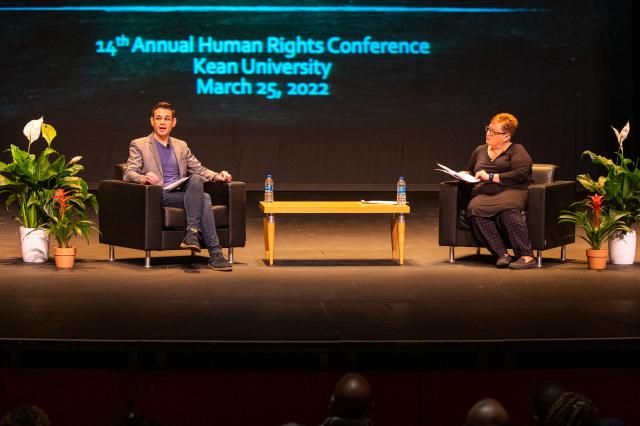 Two white people, a white man and a white woman, in business attire speaking to a crowd.