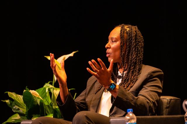 A black woman in business attire speaking to a crowd of people.