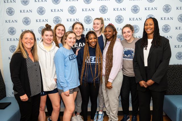 A group of students from different backgrounds who are wearing casual attire such as sweaters and leggings, standing next to a black woman in a black suit, who was the guest speaker at the HRI conference. 