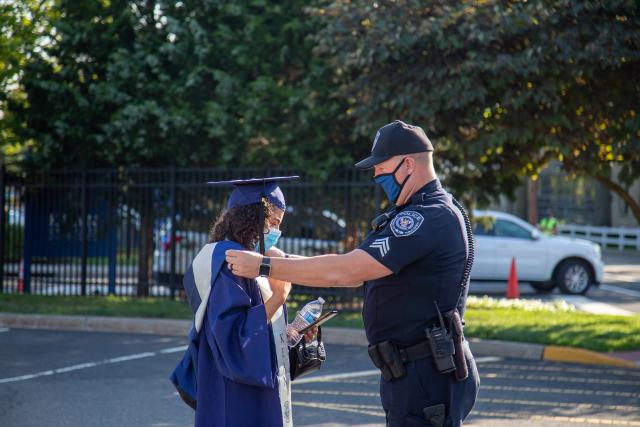 Officer helps graduate adjust her sash at commencement ceremony.