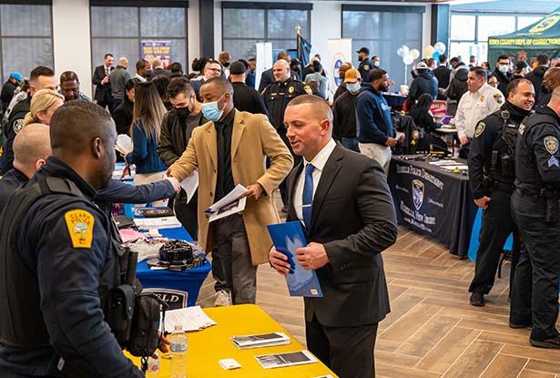 Attendees at a crowded recruitment event talk with law enforcement officers who are manning information tables.