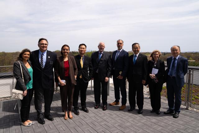 A group of individuals in professional attire, such as suits, on a balcony and smiling.