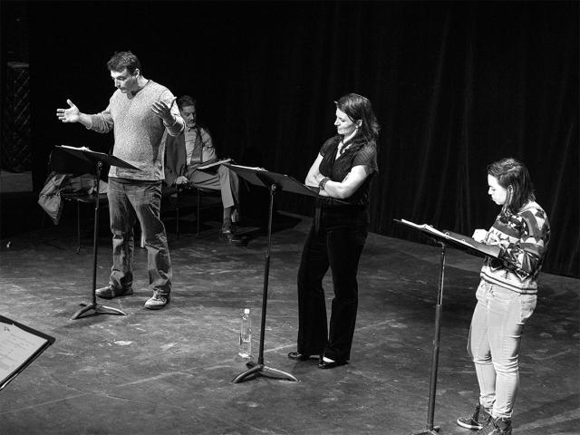 Three actors standing on stage and reading off of music stands. black and white image