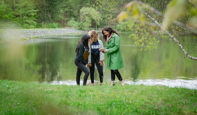 Three women wearing black leggings and light jackets laughing in front of a lake.