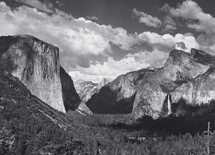 A black and white photo of a landscape of mountains over a sky filled with clouds.