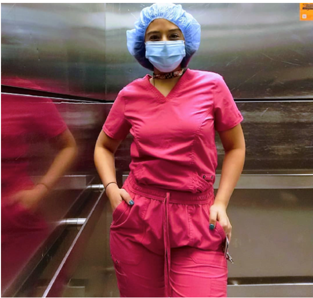 A tan Hispanic woman in bright pink scrubs with a blue mask and blue shower cap.