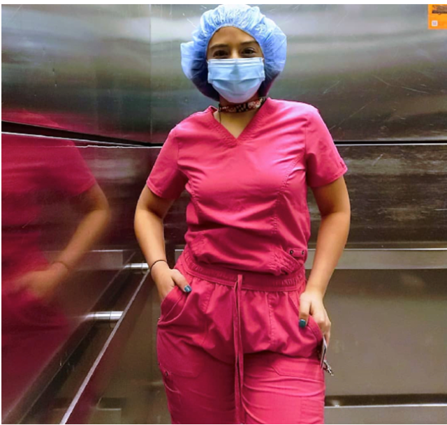 A tan Hispanic woman in bright pink scrubs with a blue mask and blue shower cap. 