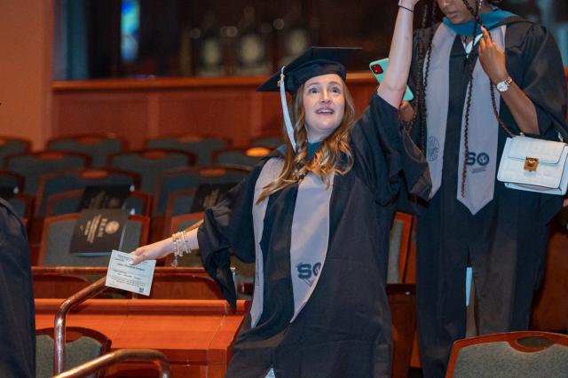A graduate in cap and gown waves to family and friends as she processes into NJPAC.