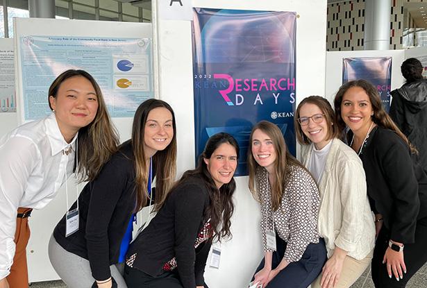 Six young women pose in front of a research poster.