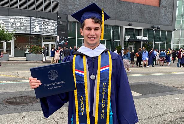 Joseph Fuca, in a blue cap and gown, holds his diploma cover outside the Prudential Center.