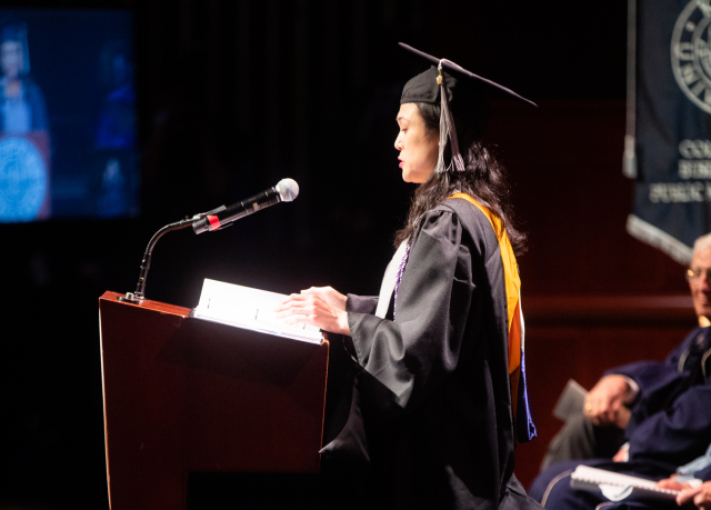 Stephanie Lo, in cap and gown, speaks at the NJPAC podium.