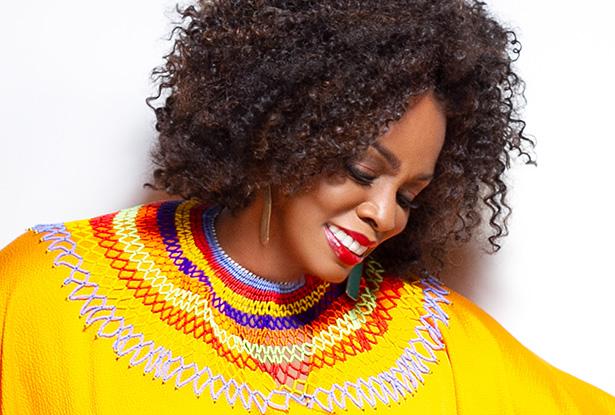 Dianne Reeves in a bright yellow blouse looks down as she smiles.
