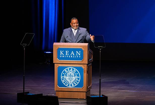 Kean President Repollet gestures as he speaks at a podium onstage at Wilkins Theatre.