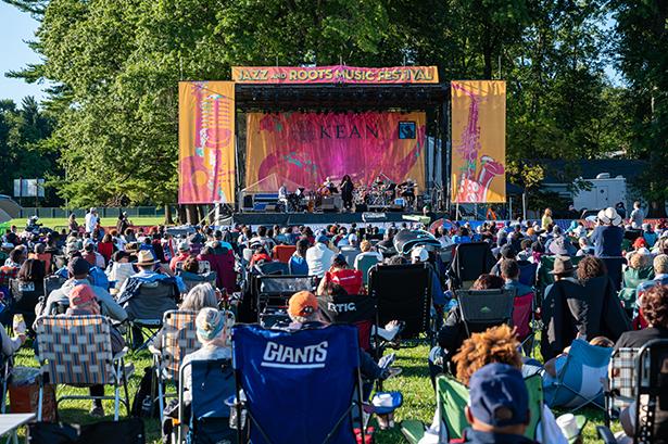 The audience at the Jazz & Roots Festival sits on lawn chairs, their backs to the camera, facing the stage.