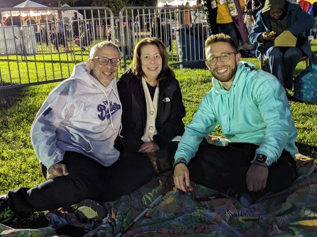 A family sits on a blanket at the Jazz & Roots Festival in the evening.