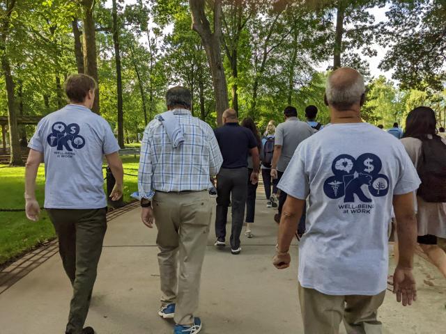 Over-the-shoulder shot of diverse men and women staff and faculty members as they walk under trees. 
