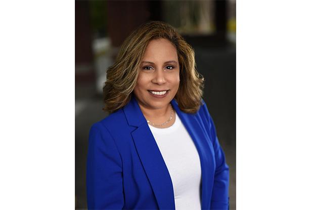 A Hispanic woman with brown hair, wearing a bright blue jacket and white shirt