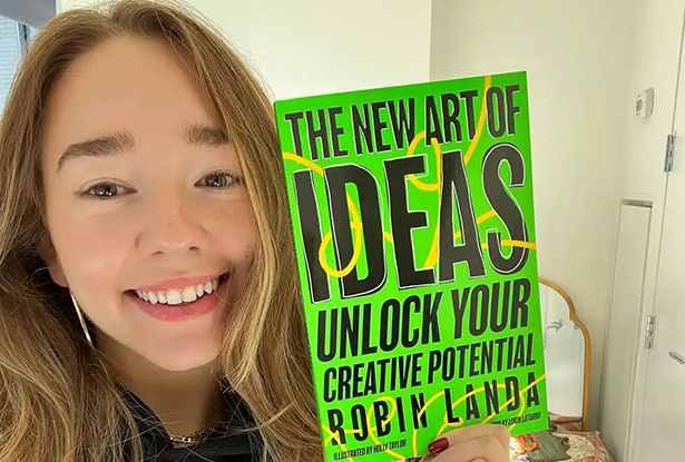 Actor Holly Taylor smiles as she holds up the book, The New Art of Ideas.