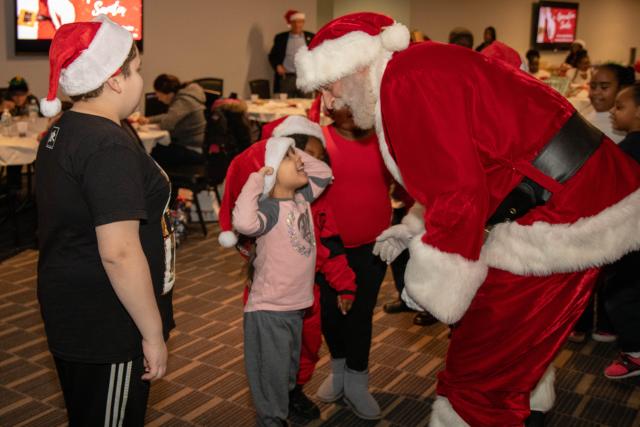 Santa Claus leans over to talk with a little boy, who is wearing a Santa hat.