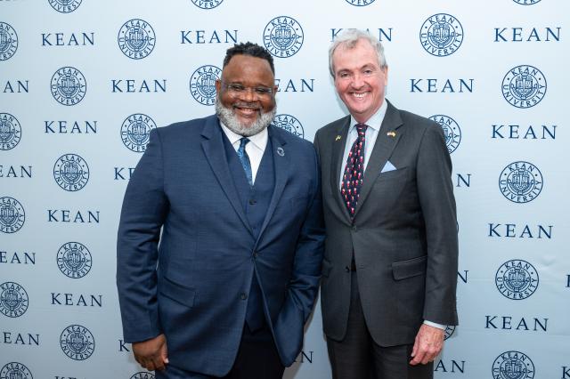 (L-R) President Lamont Repollet, a Black male with dark black hair and gray and black facial hair,  wearing glasses, a navy suit and white button-up shirt underneath and a blue and black tie. Next to him is Governor Phil Murphy, a white male with gray hair, wearing a gray suit and light blue button-up and navy blue tie with Santa Claus on them. 