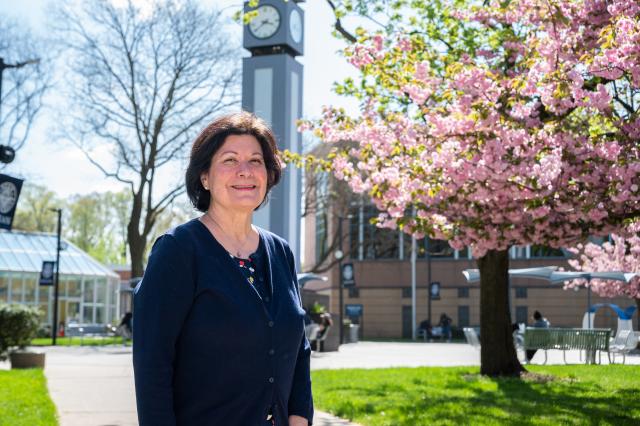 Bernie Moriarty on the Kean campus in front of the clock tower and flowering tree