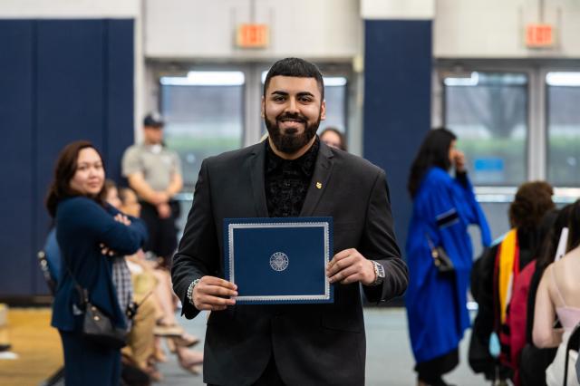 Male graduate holds honors certificate and smiiles