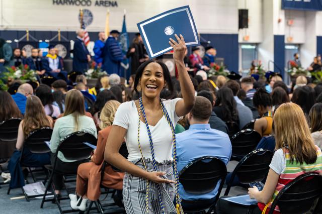 Smiling woman graduate holds her honors certificate aloft