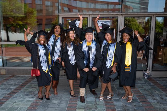 A group of Kean students in graduation caps and gowns celebrates outside NJPAC.