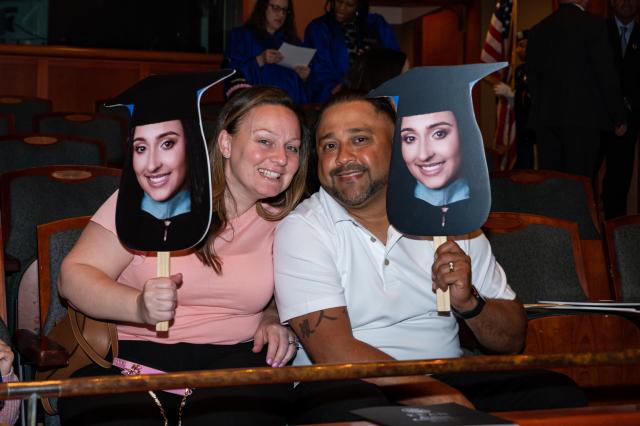 Happy parents hold oversized photos of their graduates