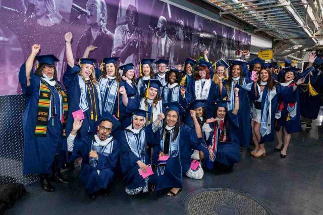 A group of Kean graduates in blue caps and gowns cheer.