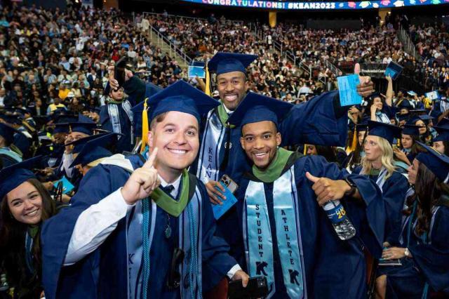 Three young men in blue caps and gowns celebrate at Kean's 2023 commencement.