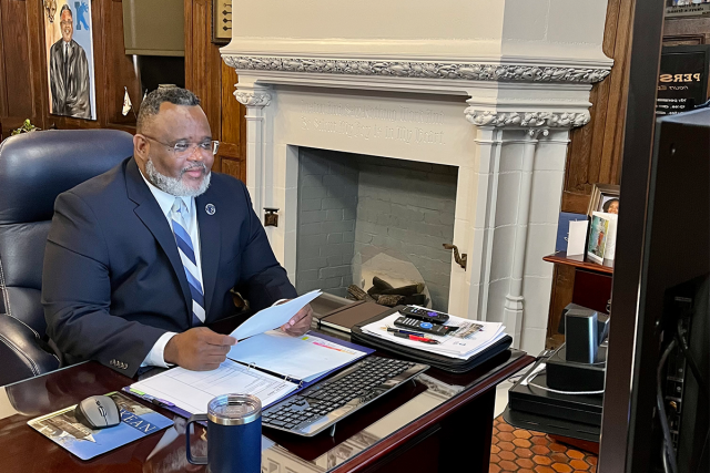 Kean President Repollet at his desk before a large computer monitor testifying at a Congressional briefing
