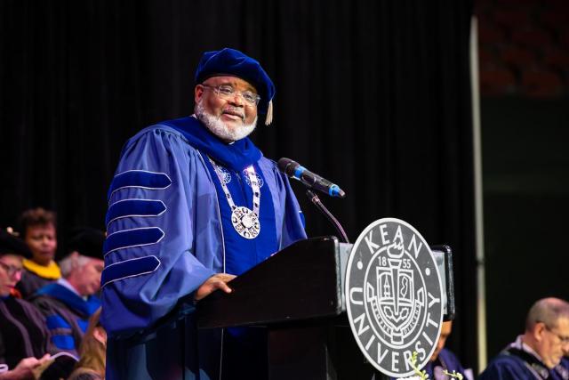 Kean President Repollet in a blue commencement gown and cap speaks at a podium.