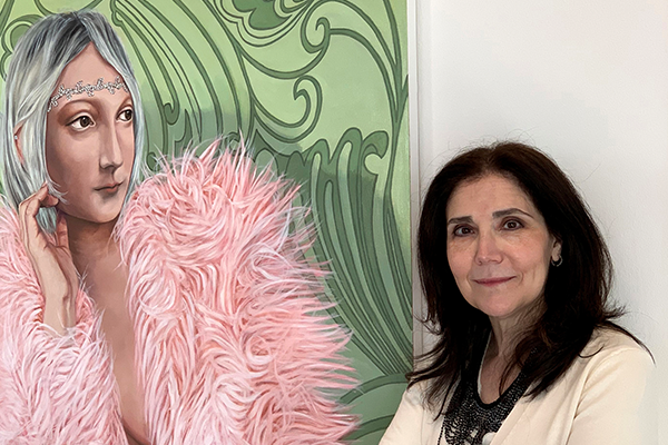 Artist Lisa Ficarelli-Halpern stands before a painting of a woman, with gray hair and pink boa.