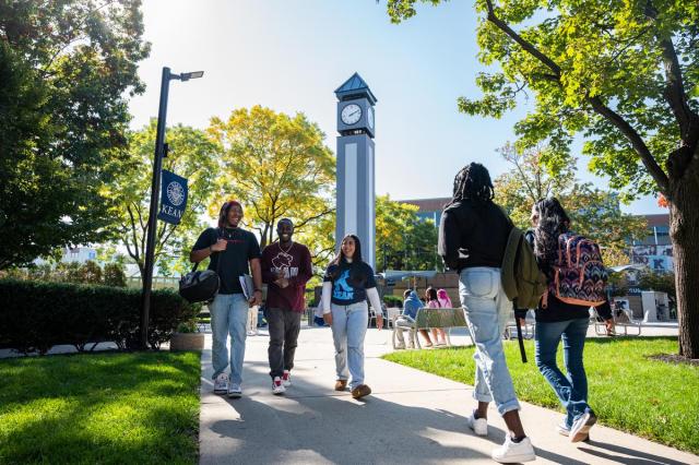 Five students walk on Kean's Union campus, with the blue clock tower in the background.