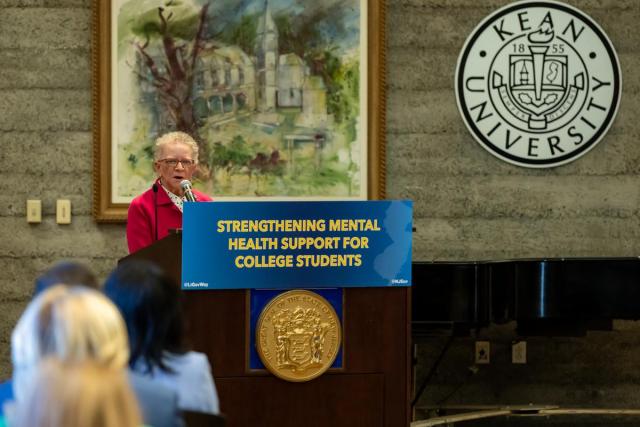 Assemblywoman Mila Jasey, at a podium with the sign Strengthening Mental Health Support for College Students