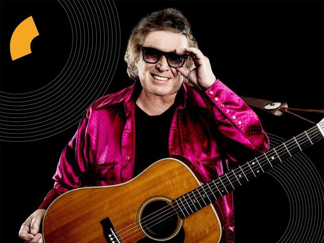 White male with glasses, smiling, holding a guitar.