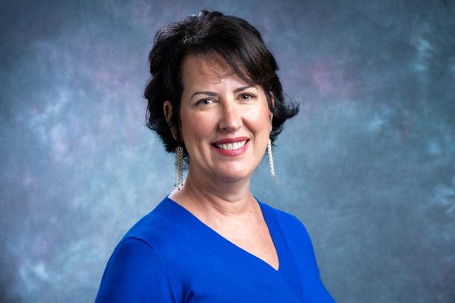 Headshot of a smiling white woman with short dark hair, wearing a blue blouse.